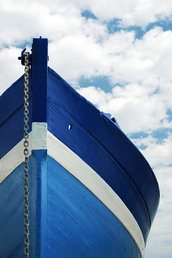 Front view of a wooden white and blue row fisherman boat under a cloudy sky.