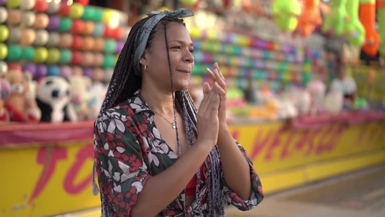 Happy video of an African American woman dancing outside at amusement park, smiling and clapping.