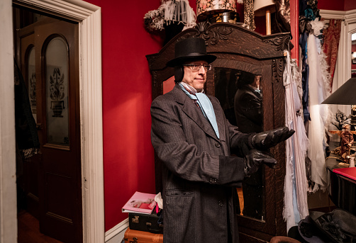 Mature man getting dressed for Christmas carolling,  He is dressing up in period costume. Interior of vintage home during evening.