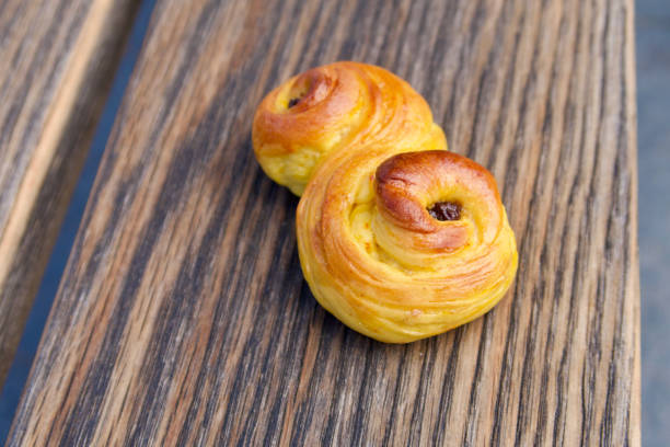 A homemade traditional yellow saffron bun lies on a brown piece of textured wood.