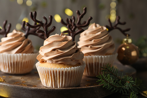 Tasty Christmas cupcakes with chocolate reindeer antlers on wooden tray, closeup