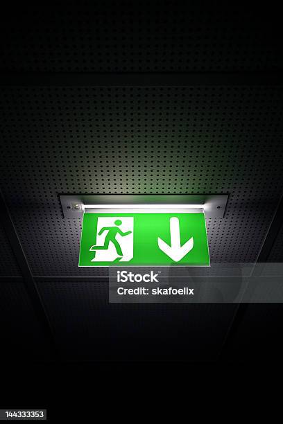 Green Illuminated Emergency Exit Sign On A Dark Hallway Stock Photo - Download Image Now