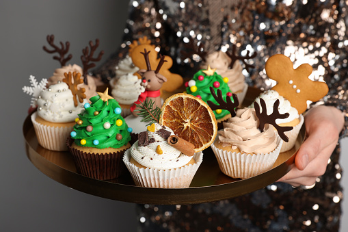 Woman holding tasty Christmas cupcakes on light background, closeup