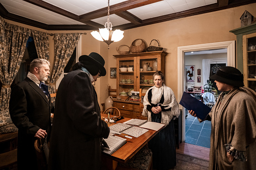 Mature people practising singing for Christmas carolling.  They are dressed up in period costumes. Interior of vintage home during evening.