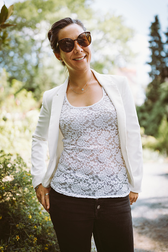 Beautiful young happy multiracial Asian business woman in white blazer, lace shirt, jeans and sunglasses in summer park, smiling