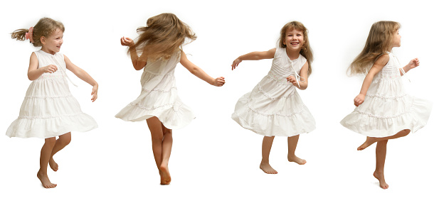 The Small girl in white gown spins, jumps, playing, smiling,  pose on white background.