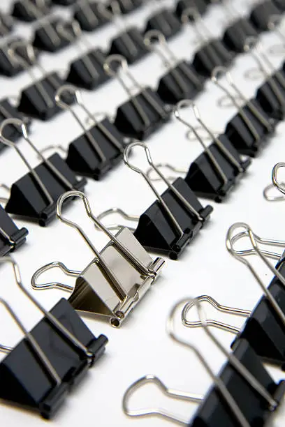 Rows of identical binder clips with a single unique one standing out from the crowd.