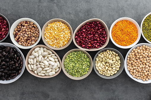 Different types of legumes in bowls, yellow and green peas, mung beans and chickpeas , colored beans and lentils, top view, copy space
