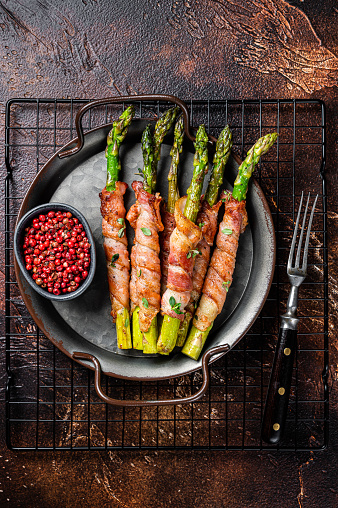 Baked Prosciutto wrapped green asparagus. Dark background. Top view.