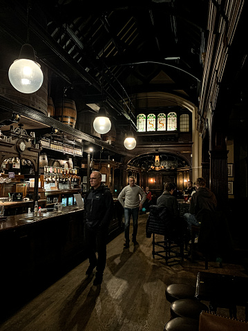 Inside of old charming pub Cittie of Yorke in Holborn, central London at High Holborn street. cozy pub with oak casks high at the ceiling for decoration. People are drinking beer by the bar after job.
