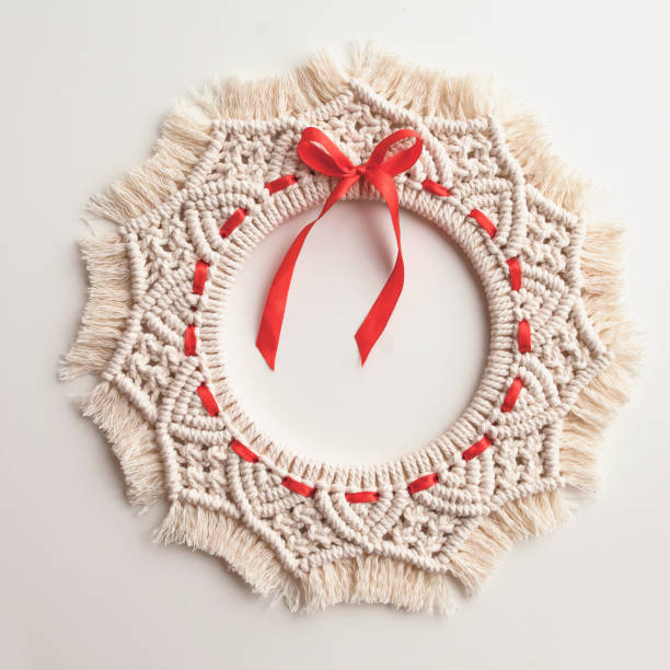 Christmas decor. Macrame wreath for Christmas and the new year on a white background. Natural cotton thread, red tape. Eco decor for home. stock photo