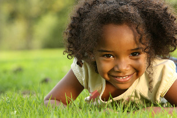 Young girl with dark skin lying down in a field stock photo