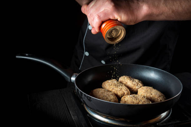 istock Cooking cutlets on grill pan by chef hands on black background for copy space text restaurant menu. The chef adds pepper 1443351956