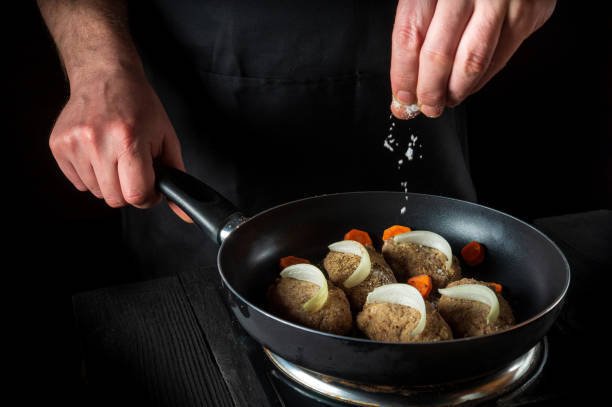 istock Cooking cutlets on grill pan by chef hands on black background for copy space text restaurant menu. The chef adds salt 1443351998