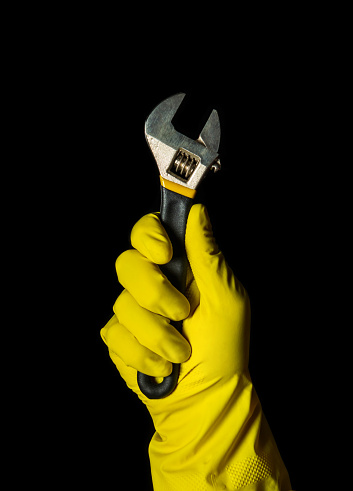 Worker hand in yellow glove holds adjustable wrench on a black background. Idea for building or renovation.