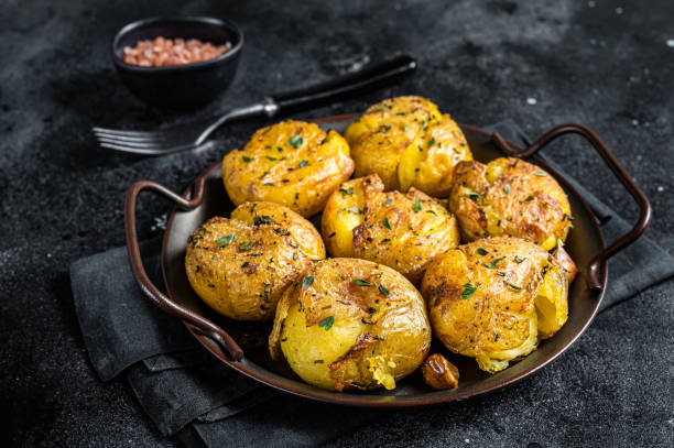 broken potatoes baked in oil with herbs. black background. top view - smashed potatoes imagens e fotografias de stock