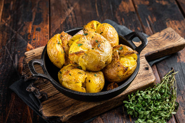 crushed, broken potatoes baked in oil with herbs. wooden background. top view - smashed potatoes imagens e fotografias de stock