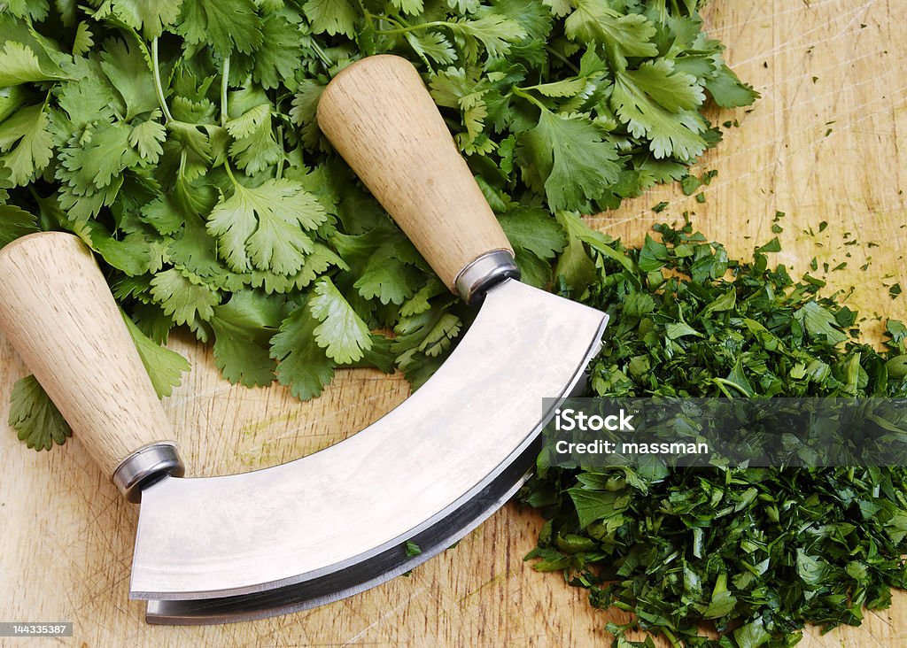 mezzaluna and herbs fresh and chopped herbs on cutting board with a mezzaluna Chopped Food Stock Photo