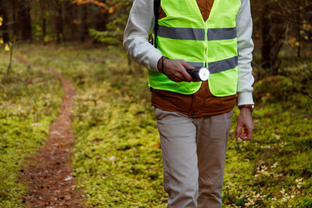 Male Volunteer of the Search and Rescue Team Dressed in a Signal Vest with a Flashlight in the Forest. stock photo
