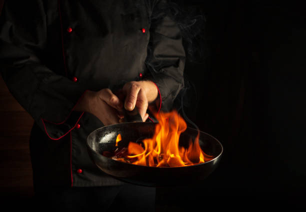 istock Professional chef cooking food in pan with fire flame on black background. Restaurant and hotel service concept. European cuisine 1443354974