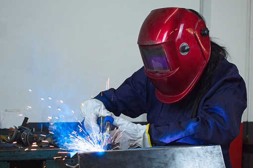 Male welder wearing helmet working with welding torch in factory.