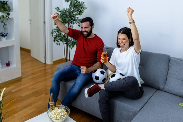 istock A cheerful young couple is watching a soccer game at home. 1443355593