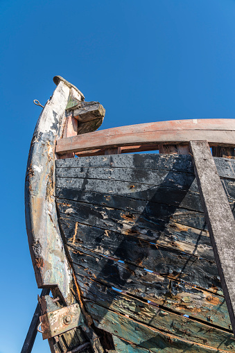 Front part of old, ruined wooden boat against blue sky, low angle view.