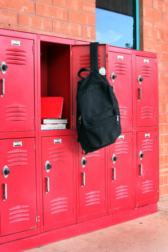 Books inside of a school locker with a black backpack hanging on the door.