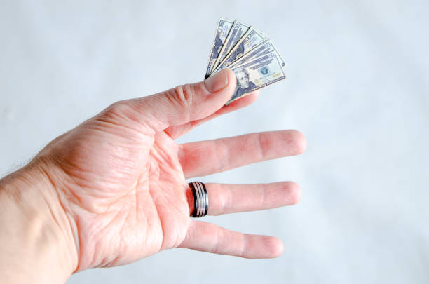 Hand holding tiny 20 dollar bills to represent loss of spending power on white background.\nThis is to represent shrinkflation, the fact that, to make more money, the manufacturers are reducing the package and keeping the same price of goods.\nThe consumers are then losing spending power.