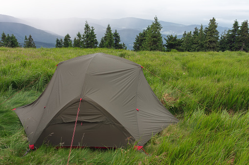 Green lightweight freestanding three-season 2-person tent on mravenecnik hill in grass in the morning after rainstorm