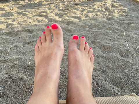 Female legs, feet with a beautiful red pedicure on the background of sand on vacation on the beach in a warm tropical eastern paradise country southern resort.