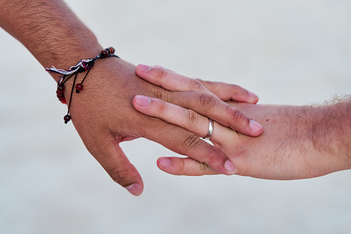 portrait of two intertwined men's hands of a homosexual couple on an out of focus background, lgtbi concept.