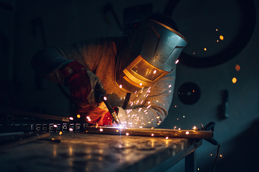 Man worker working with a metal product and welding it with a arc welding machine in a workshop. Industrial manufacturing. Welding metal part in a factory. Orange sparks. Copy space.