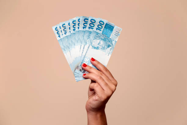 one hundred reais banknotes - hand holding brazilian banknotes several hundred real bills - money from Brazil in a womans hand with red nails banknote stock pictures, royalty-free photos & images
