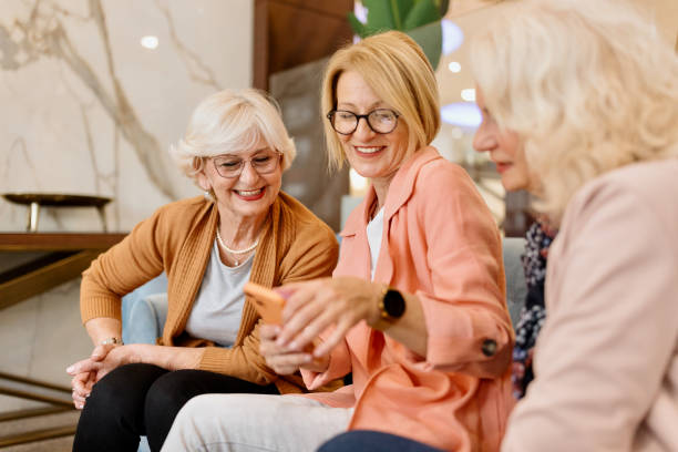 amigas seniores sentadas no café do hotel usando smartphone - hotel restaurant women luxury - fotografias e filmes do acervo