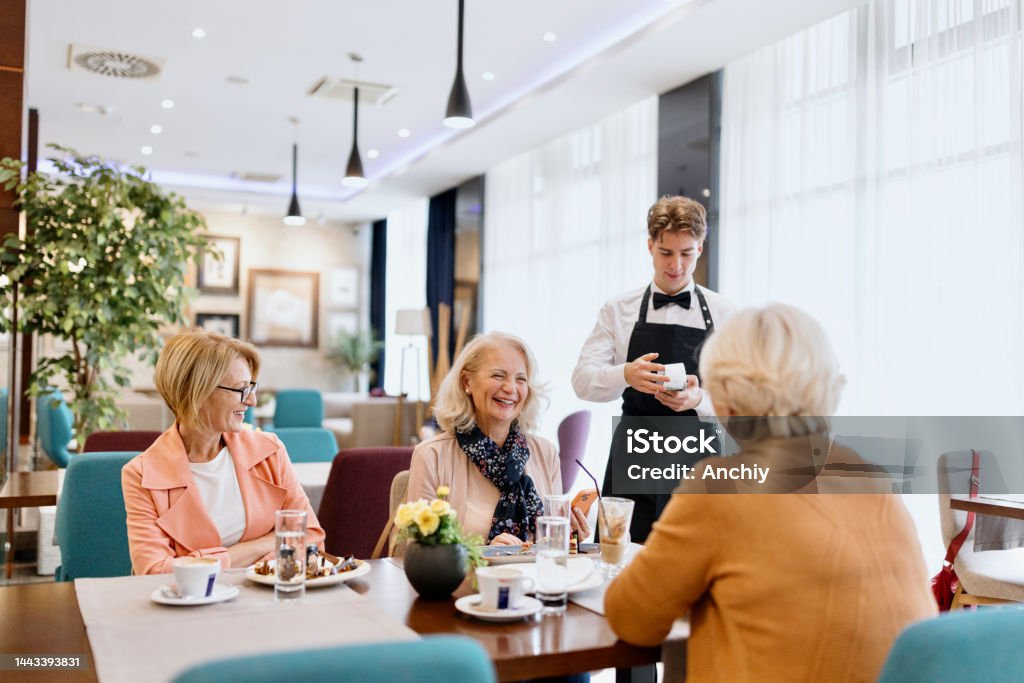 Senior woman making a contactless payment at a restaurant using her cell phone Cheerful senior female friends having tasty dessert and talking in cafe Dining Stock Photo