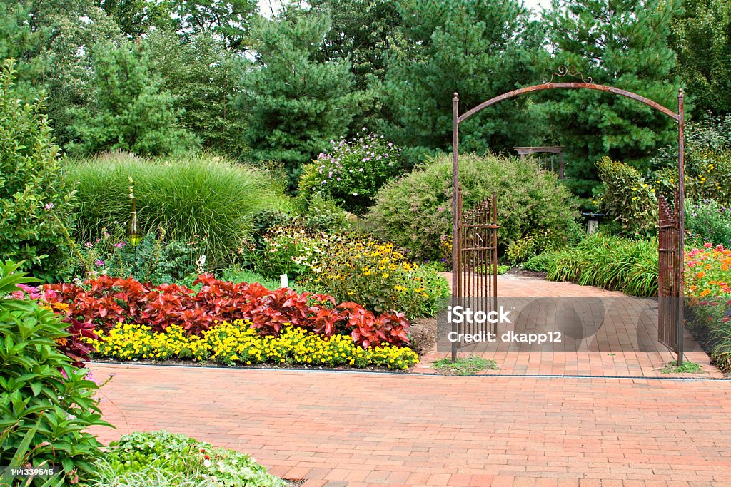 Formal garden with red brick pathway and rustic open gate A formal garden complete with iron gate and paving brick pathway. Brick Stock Photo