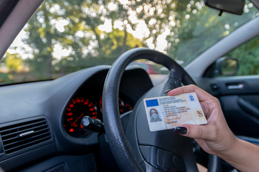 Teenager girl  showing his driver's license in the car window after passing the exam or at the request of the traffic police