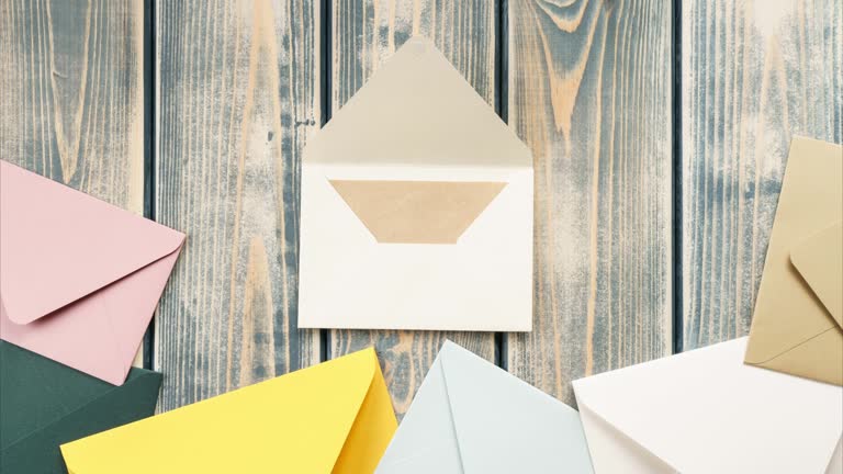 White opening envelope on wooden background. Multicolored envelopes fall from above, kraft paper card opened. Copy space