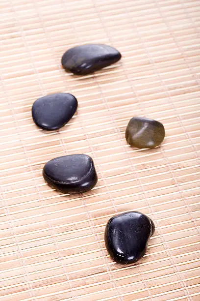 Five smooth, black Zen-Stones (Pebbles) in a row on a bamboomat. Focus on front stone.