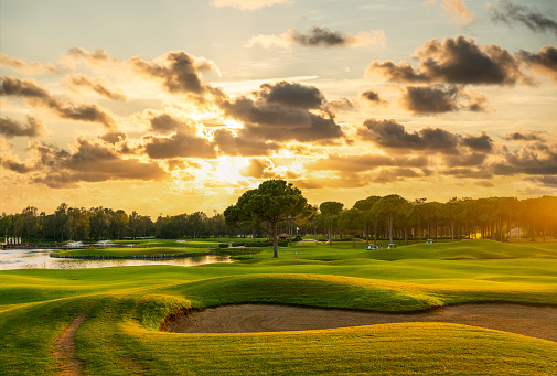 Drone perspective view of two golfers lining up their putts. They are in the beautiful surroundings of a golf course on the island of Moen in Denmark, surrounded by sand traps and water features. Horizontal format with some copy space.