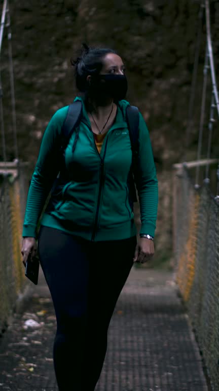 Brunette woman wearing face mask and filming with smart phone while walking in the forest.