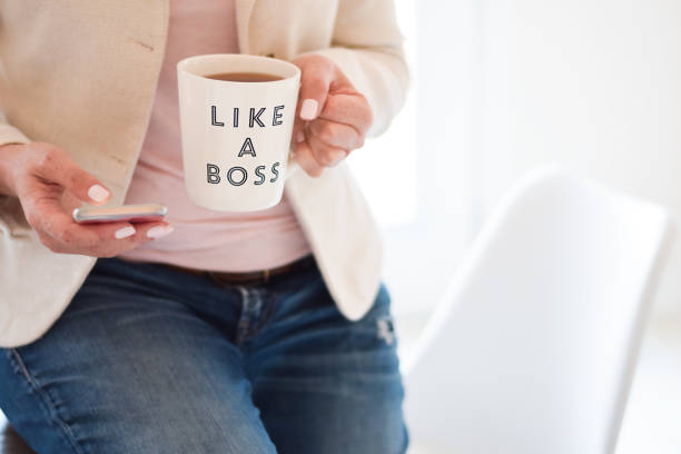 Business woman using mobile phone and holding cup that says Like a Boss