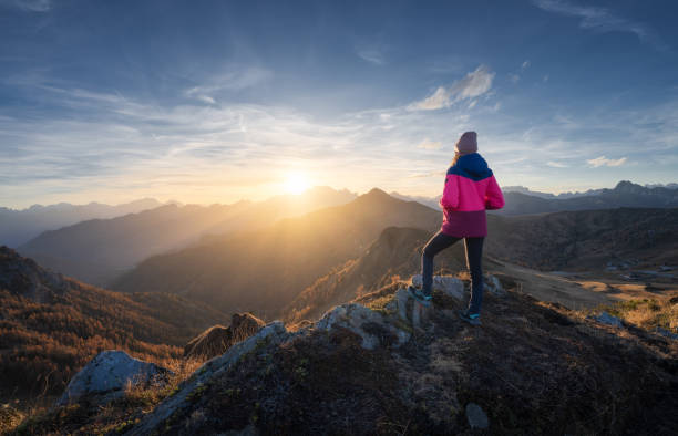 jeune femme au sommet de la montagne et de belles montagnes dans la brume au coucher du soleil coloré en automne. dolomites, italie. fille sportive, crêtes de montagne dans le brouillard, herbe orange, arbres, soleil doré à l’automne. randonnée - couleur panachée photos et images de collection