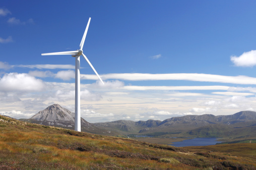 Wind turbine in rural location with lake and mountains in the background.