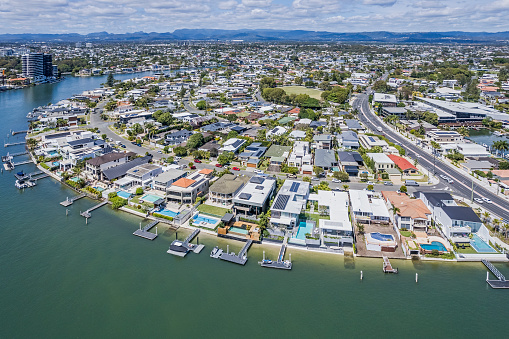 Aerial view Nerang River Housing estate (Isle of Capri) with urban sprawl and Hinterland in background. Luxury waterfront houses with swimming pools, private boat moorings & piers. Wide angle, higher elevation