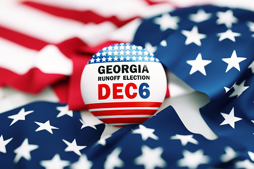 Georgia Runoff Election Dec 6 written badge sitting over rippled American flag. Great use for election and voting concepts. Georgia runoff election concept. High angle view.