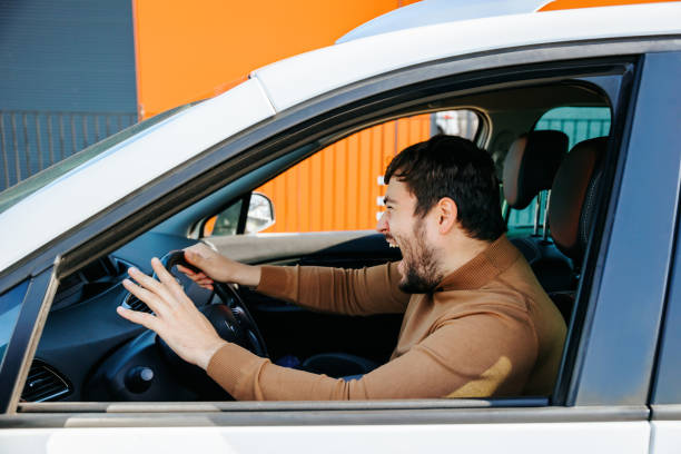 middle-aged caucasian caucasian man is inside the car and is yelling furiously. the middle-aged caucasian male chauffeur is inside the car and is yelling furiously. male with open mouth stressed and gesturing with hands. Side profile mouth open men screaming shouting stock pictures, royalty-free photos & images