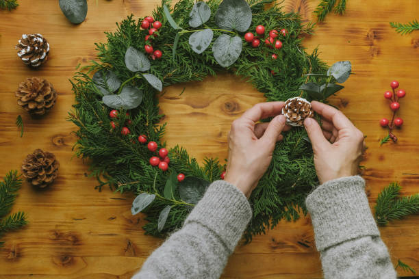 istock Young woman decorating handmade Christmas wreath with pine cone. 1443447977