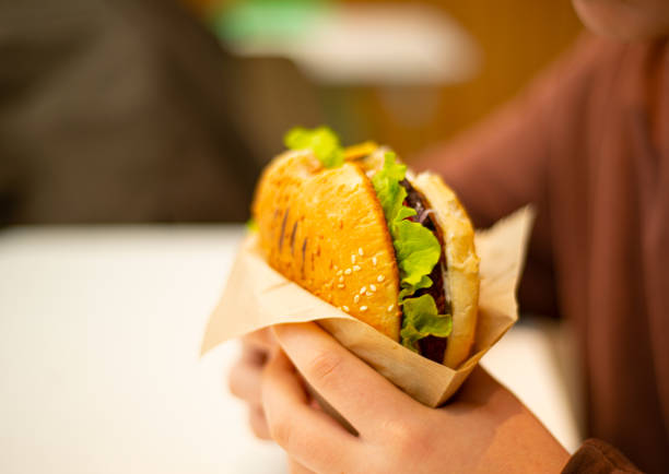 istock Burger in hand. Bun with sesame seeds. Green leaf lettuce. Vegetables and cheese. 1443450595